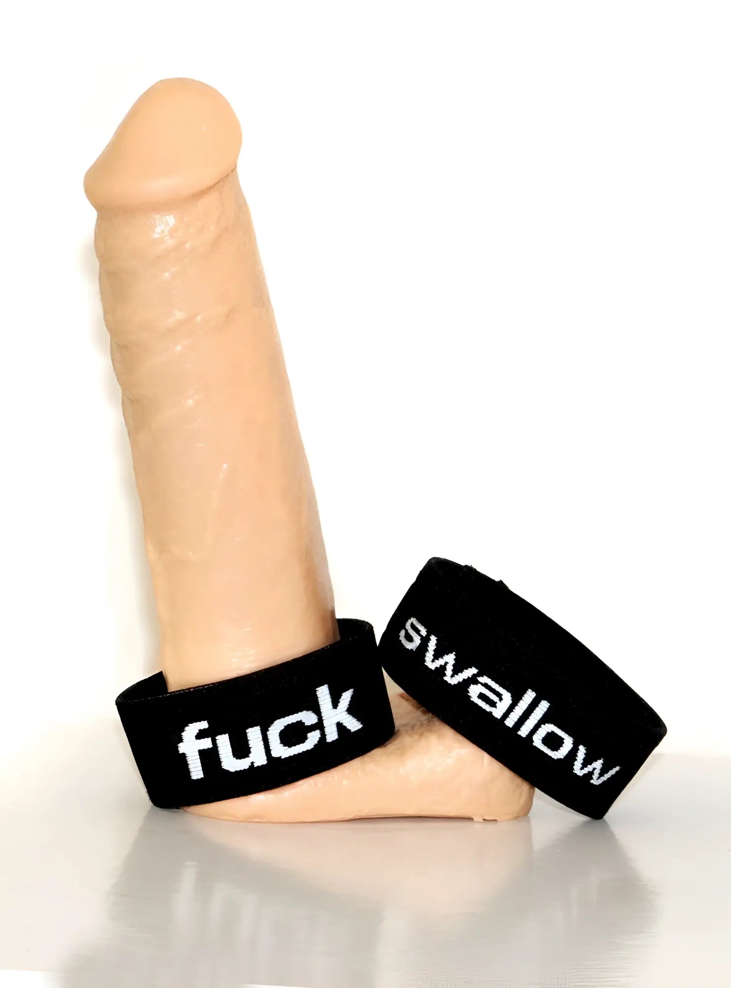 Flesh-toned phallus display base featuring two black elastic rings with white embroidered text "fuck" and "swallow".