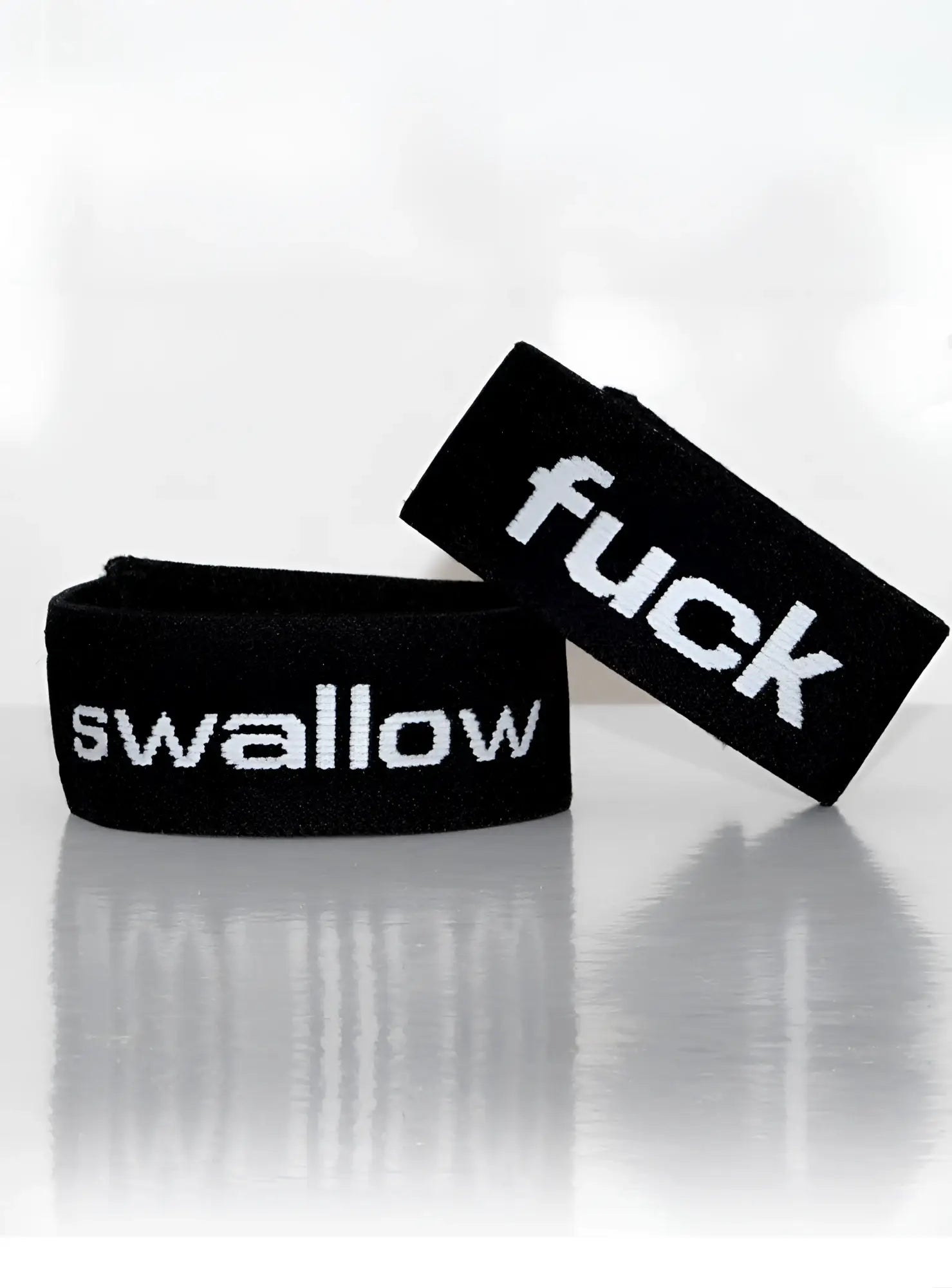 Two black elastic cock rings with white text; one says "swallow," the other says "fuck" in a bold, sans-serif font.