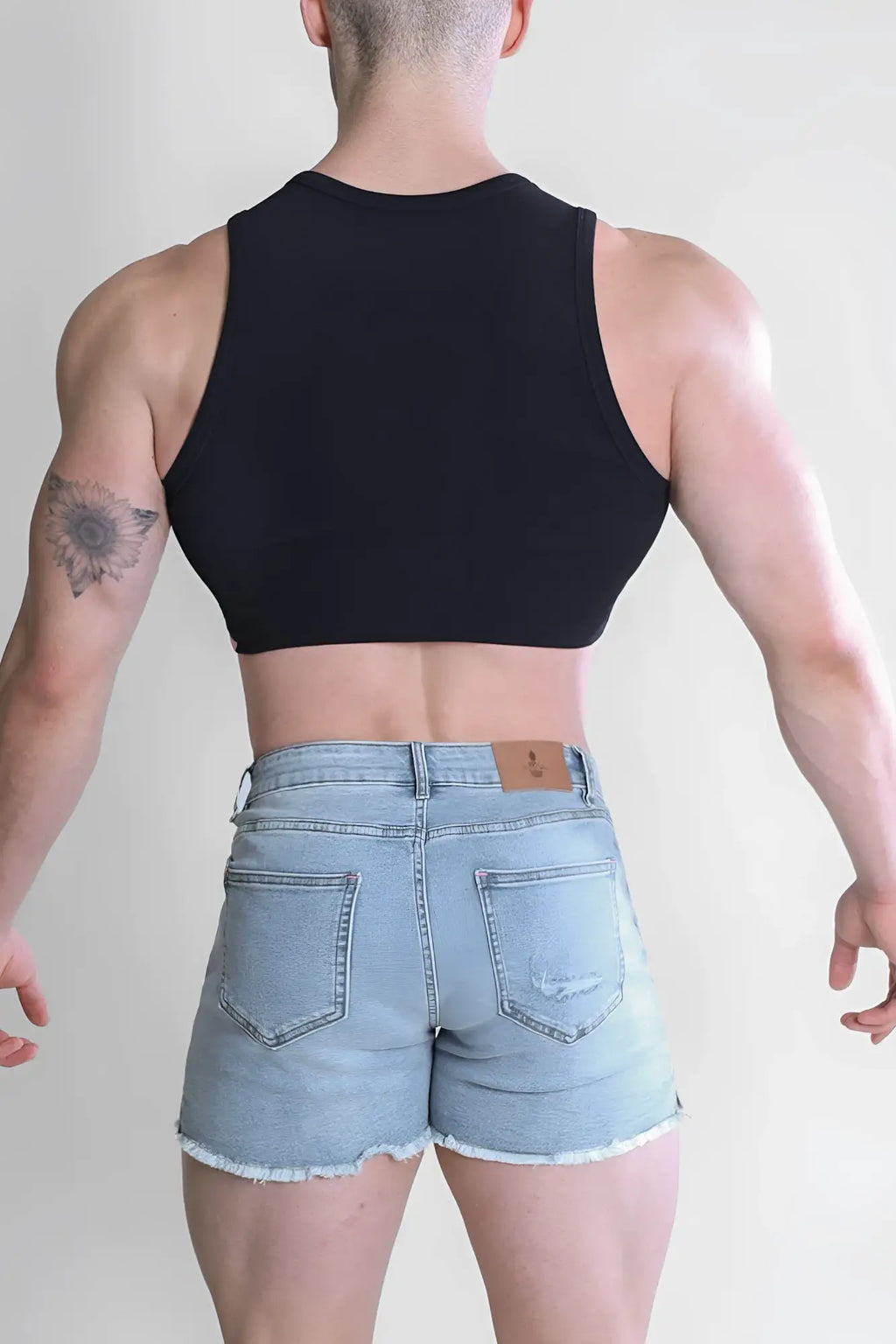 Back side of light-wash denim shorts with frayed hem and pockets paired with black ribbed crop tank wrapped up