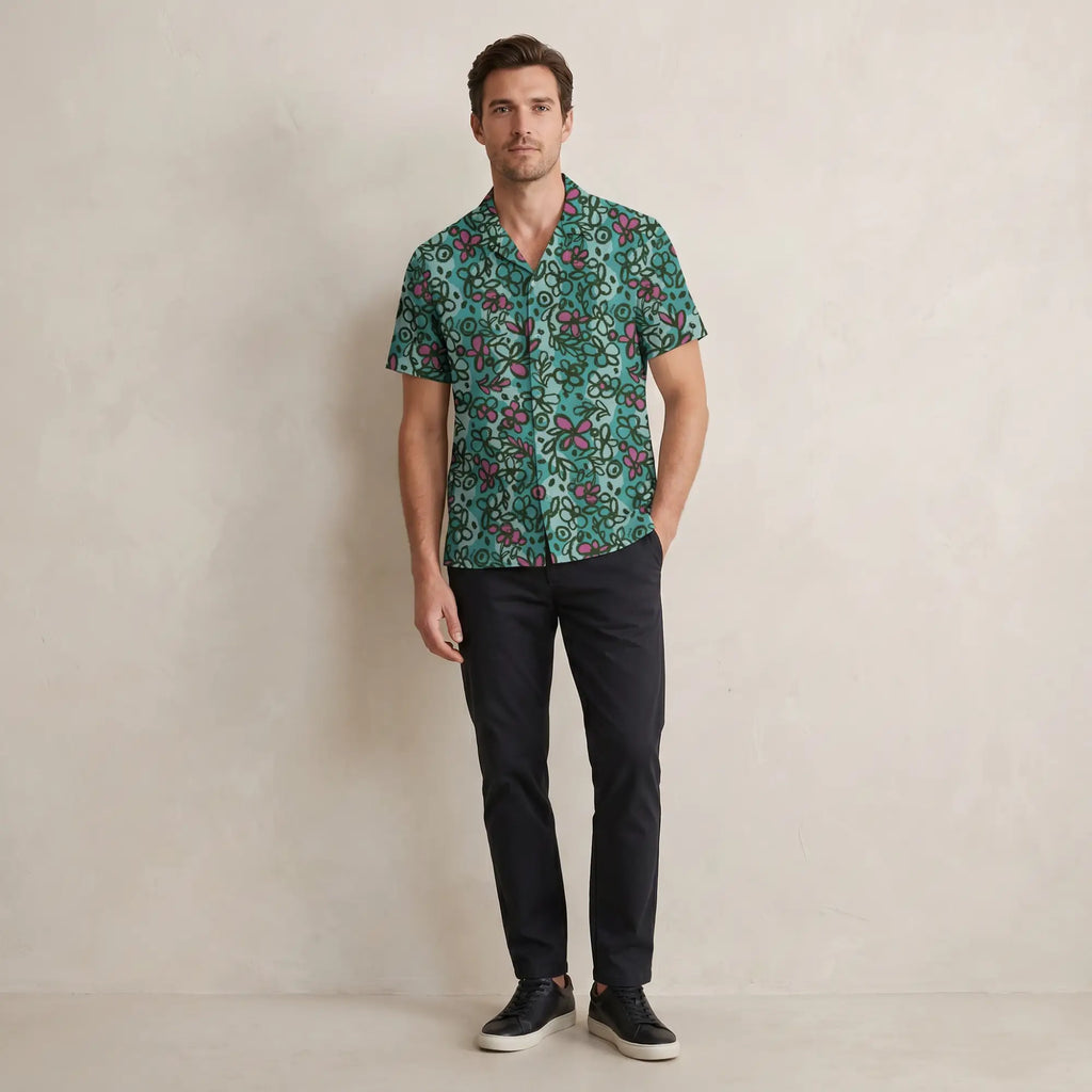 Man wearing teal Yuasa Sketchbook Cosmos short-sleeve shirt against a neutral wall, soft natural daylight.