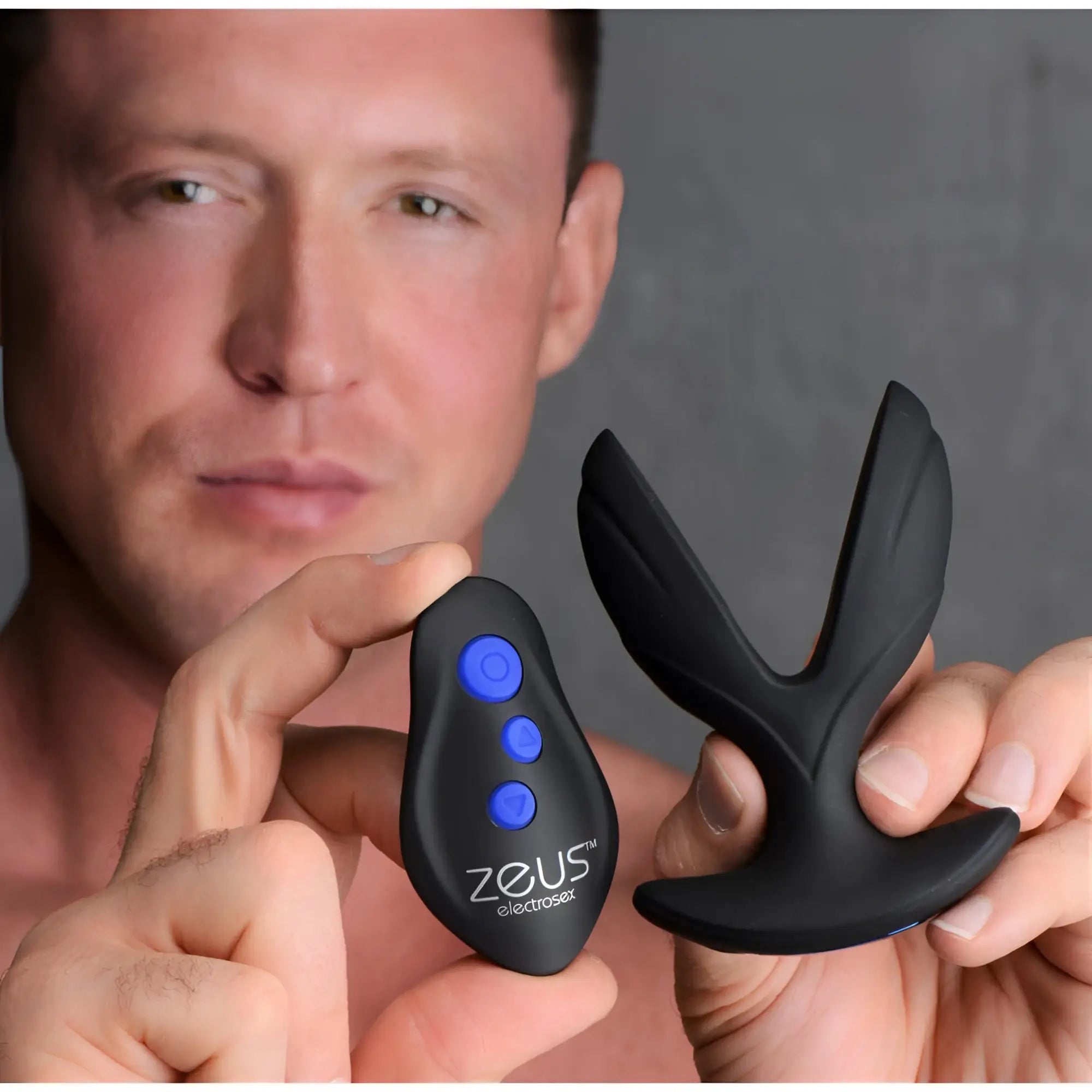 A man holding the black Zeus Electro-Spread vibrating butt plug and its matching remote with blue control buttons.