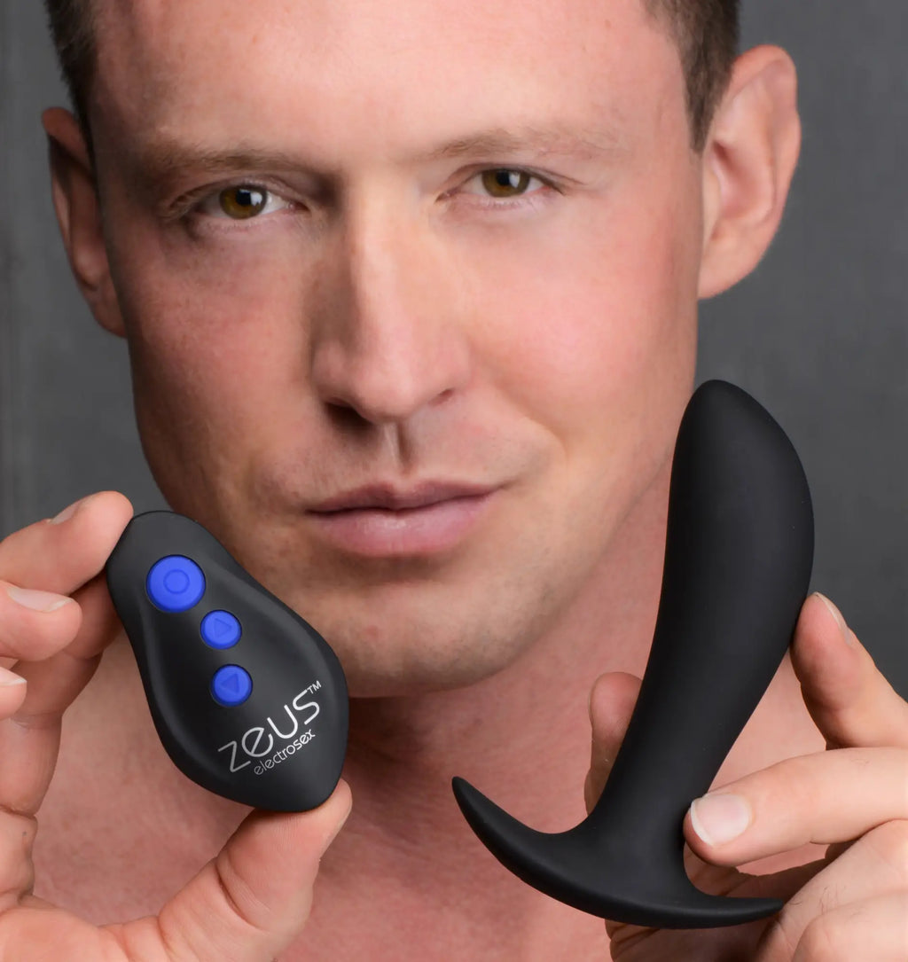 A man holds a black Zeus Electrosex 64X Pro-Shocker vibrating prostate plug and its matching remote with blue buttons.