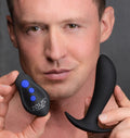 A man holds a black Zeus Electrosex 64X Pro-Shocker vibrating prostate plug and its matching remote with blue buttons.