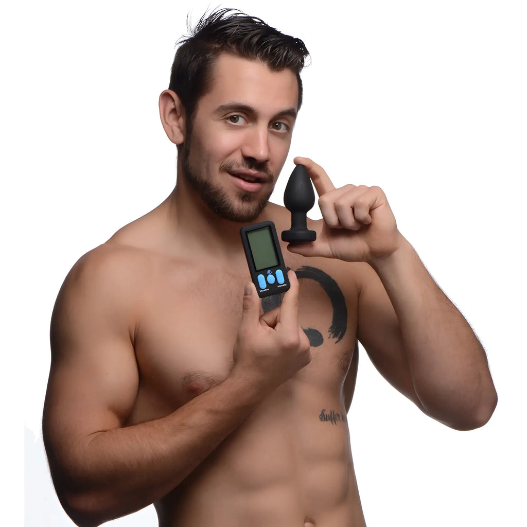 Man holding a black Zeus Electrosex E-Stim Pro vibrating anal plug and a digital remote control against white background.
