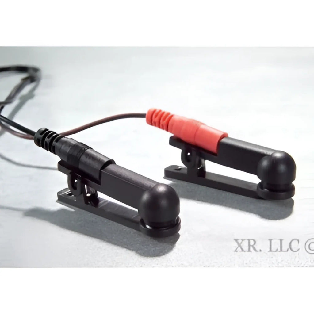 Zeus Electro Sex Clamps: Two black plastic clamps with red and black electrical lead wires on a light background.