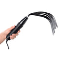 A hand holds a black Zeus Electrosex Extreme Twilight silicone flogger eStim attachment with a cord, on white.