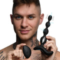 A man holding black, silicone Zeus Shock-Beads with E-stim effects and a matching remote control.